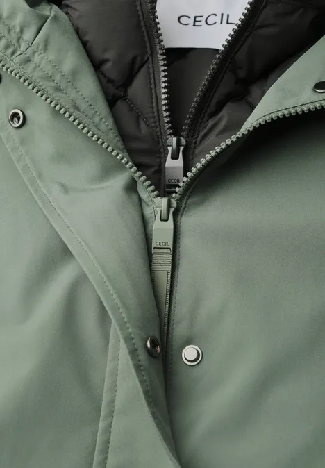 Close-up van een groene jas met ritssluiting en drukknopen, binnenvoering zichtbaar.