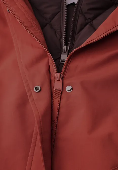 Nahaufnahme des Reißverschlusses einer rostfarbenen Jacke mit Druckknöpfen und gestepptem Futter.