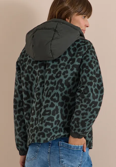 Rückenansicht einer Frau in grüner Jacke mit Leopardenmuster und Kapuze, dazu Jeans.
