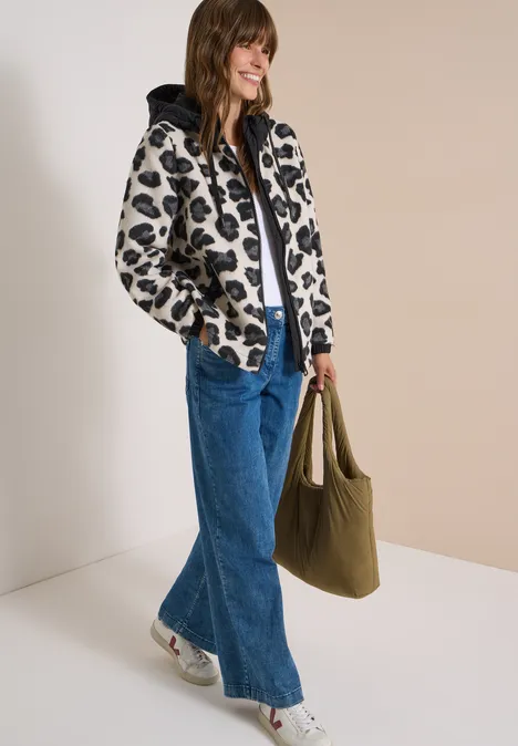 Jacke mit Wollanteil und Leo-Muster Black Frau in modischer, bedruckter Jacke, weitem Jeans, weißen Sneakers und grünem Shopper vor neutralem Hintergrund.