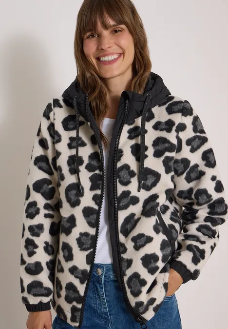 Jacke mit Wollanteil und Leo-Muster Black Frau lächelt in flauschiger, schwarz-weißer Fleckenjacke mit Kapuze vor neutralem Hintergrund.