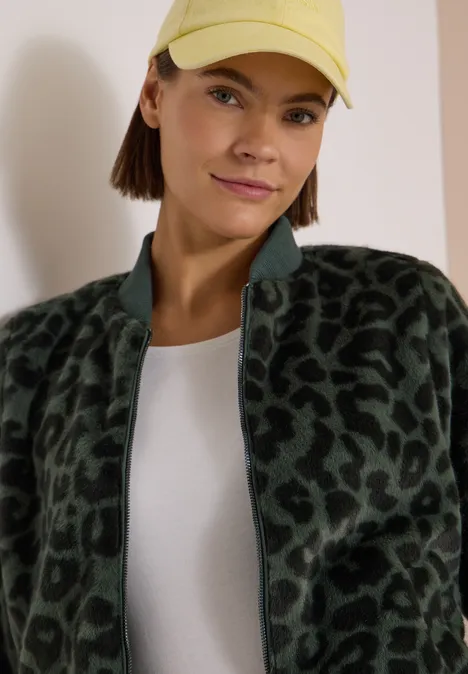 Eine Frau mit gelber Cap, dunkelgrüner Fleecejacke mit Leopardenmuster und weißem T-Shirt.