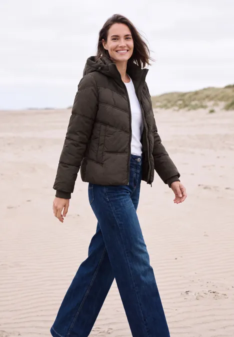 Veste matelassée à capuche avec des détails en sergé chocolate sauce brown Femme en doudoune et jean souriante, marchant sur la plage