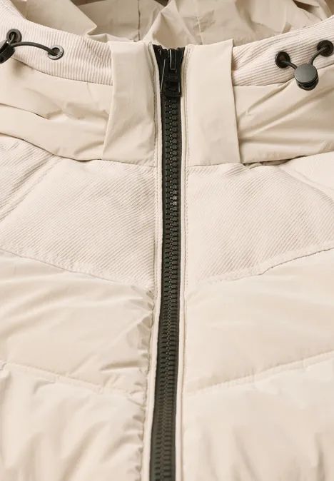 Veste matelassée à capuche avec détails en sergé powder beige Gros plan d'une doudoune matelassée crème avec fermeture éclair centrale et cordon au niveau du col.