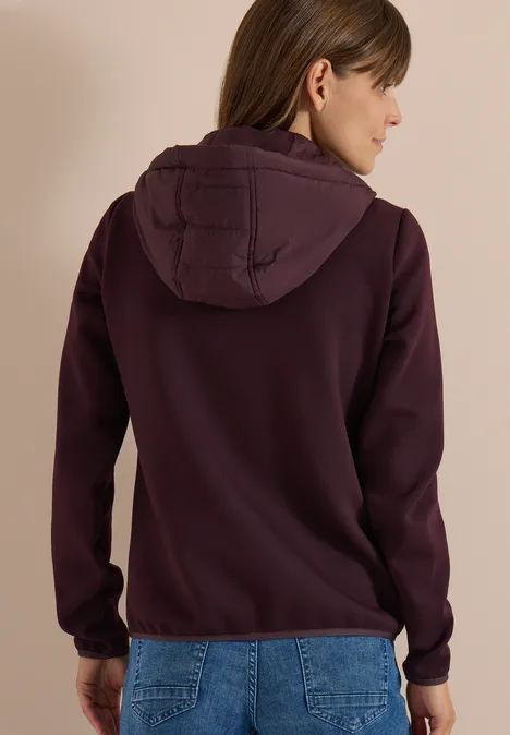 Personne de dos portant un sweat à capuche bordeaux et un jean.