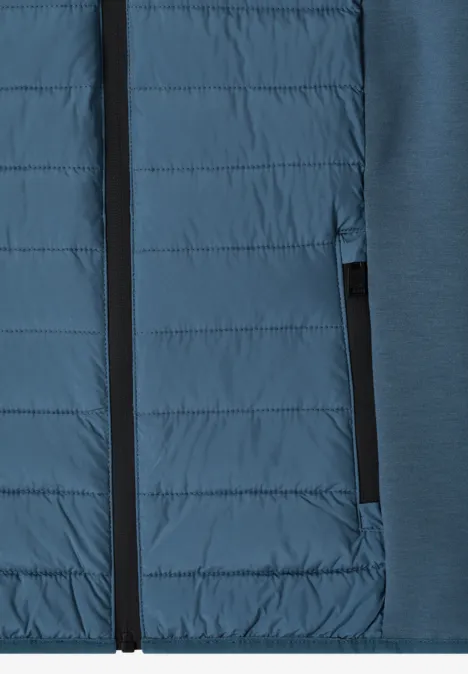 Nahaufnahme einer blauen Hybridjacke mit gesteppter Front und Reißverschlusstasche.