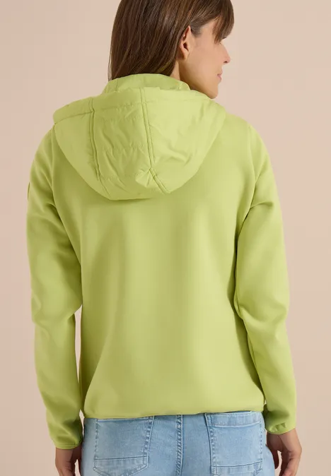 Personne aux cheveux bruns vue de dos en sweat à capuche vert clair et jean bleu clair.