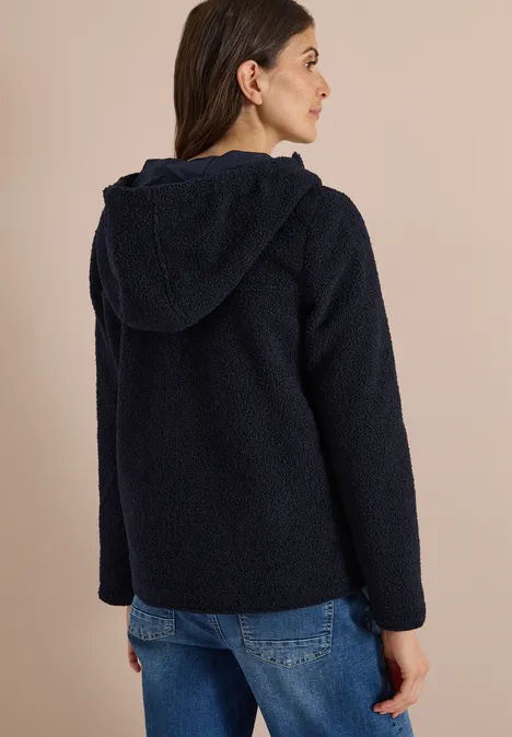 Frau von hinten trägt eine dunkelblaue Teddy-Fleece-Jacke mit Kapuze und Jeans.