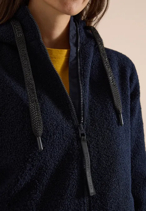 Flauschige dunkelblaue Fleecejacke mit Reißverschluss, Kordelzug und gelbem Shirt darunter.