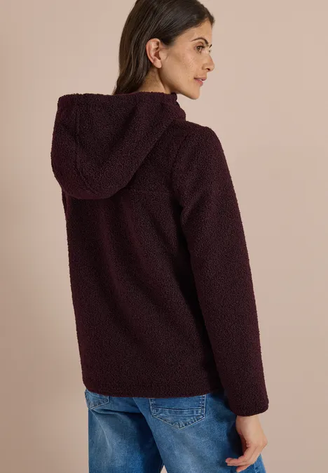 Frau im Profil, trägt eine burgunderrote Teddy-Fleecejacke mit Kapuze und Jeans.