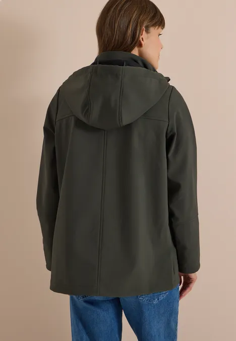 Eine Person von hinten in dunkelgrüner Kapuzenjacke und Jeans vor beiger Wand.