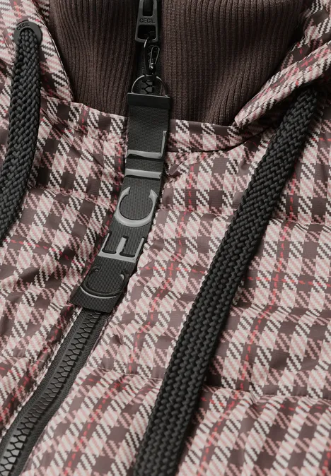 Nahaufnahme einer Jacke mit braun-weißem Hahnentritt-Muster, schwarzem Reißverschluss und Kordeln.