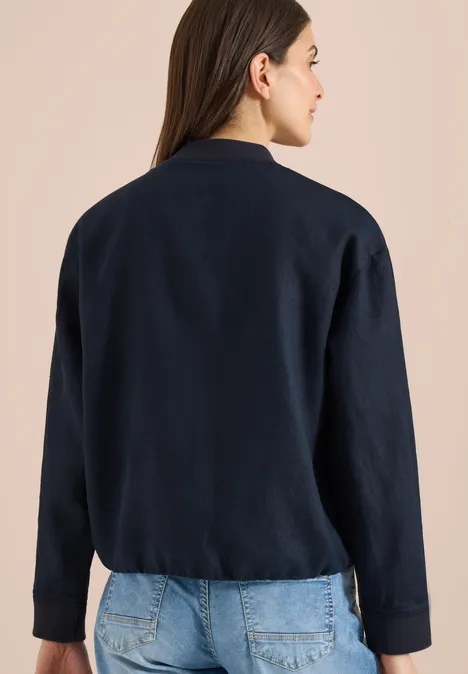 Blouson aus Leinen mit Zipper universal blue Frau von hinten in dunkelblauem Cardigan und Jeans vor hellem Hintergrund.