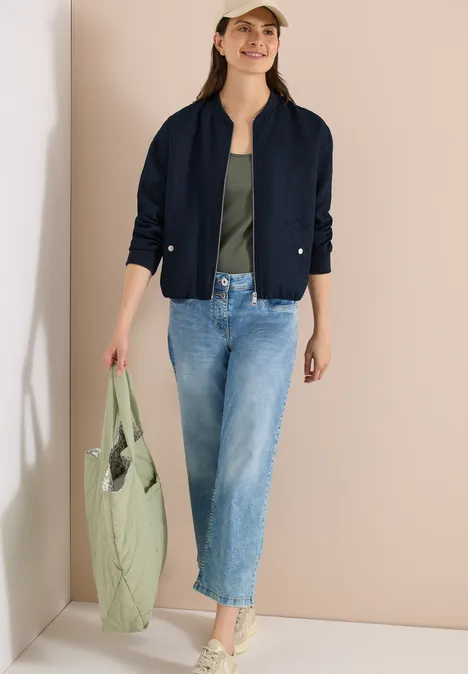 Blouson aus Leinen mit Zipper universal blue Frau in dunkelblauer Jacke, grünem Top und Jeans trägt eine große hellgrüne gesteppte Tasche.