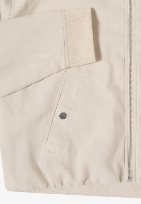 Nahaufnahme einer hellbeigen Jacke mit Reißverschluss, aufgesetzter Tasche mit Druckknopf und elastischem Saum.