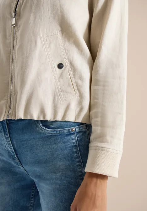 Nahaufnahme einer Person in hellbeiger Jacke und blauen Jeans, Fokus auf Rumpf und Hand.