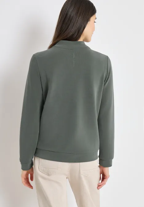 Blouson mit Zipper und Taschen khaki Frau von hinten in olivgrünem Pullover und hellen Hosen vor neutralem Hintergrund