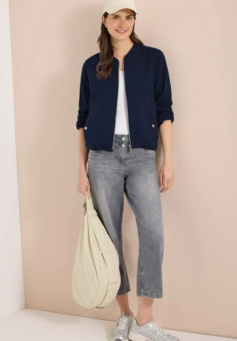Frau in modernem Casual-Look: dunkelblauer Blazer, weißes Top, graue Cropped-Jeans, weiße Sneaker, große Tasche.