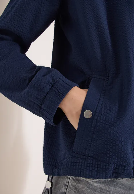 Dunkelblaue, texturierte Jacke mit verdeckter Tasche, Hand in der Seitentasche und Metallknopf