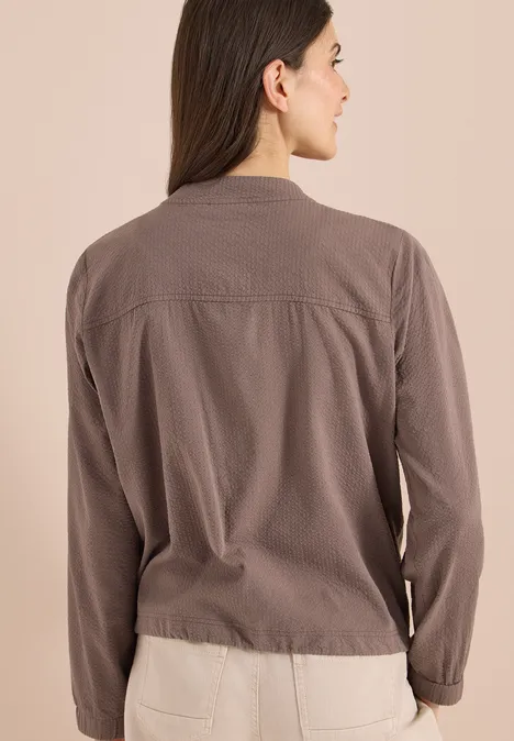 Frau von hinten in taupefarbener Jacke vor neutralem Hintergrund.