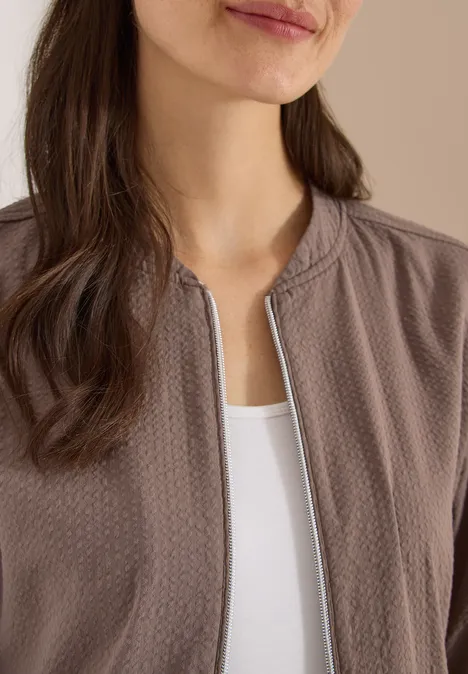 Nahaufnahme einer Frau in braunem Blouson mit Reißverschluss über einem weißen Top.