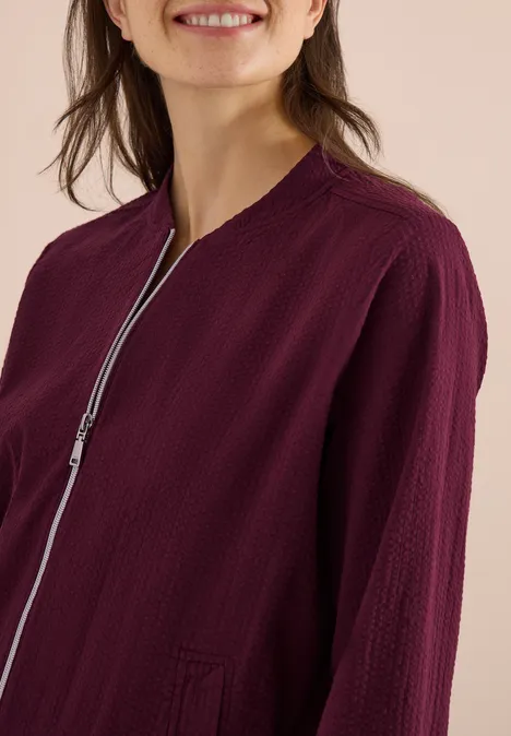 Frau in leichter, weinroter Jacke mit feiner Struktur und silbernem Reißverschluss