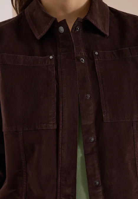 Veste en velours côtelé marron foncé avec poches avant et boutons, chemise verte en-dessous.