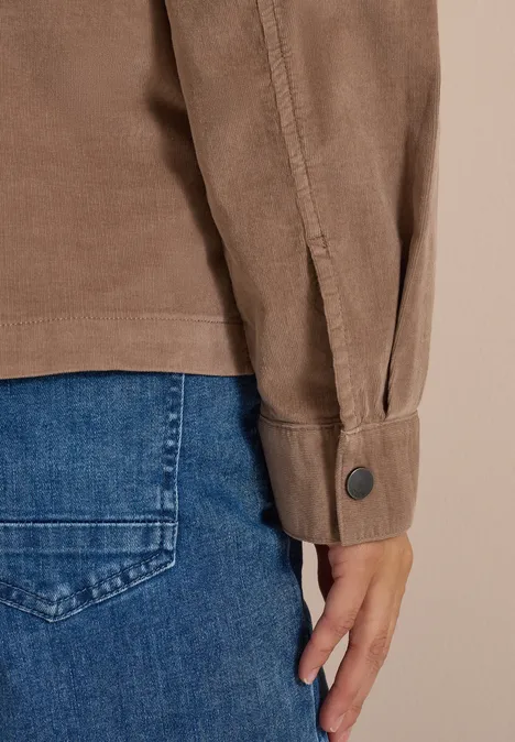 Nahaufnahme eines Arms in braunem Hemd und Hand neben der Hosentasche einer blauen Jeans.