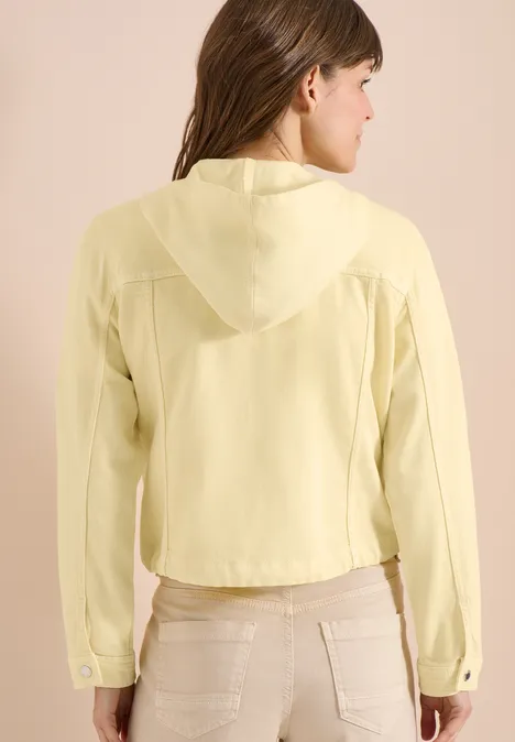 Frau von hinten in hellgelber Kapuzenbluse und beigen Hosen.