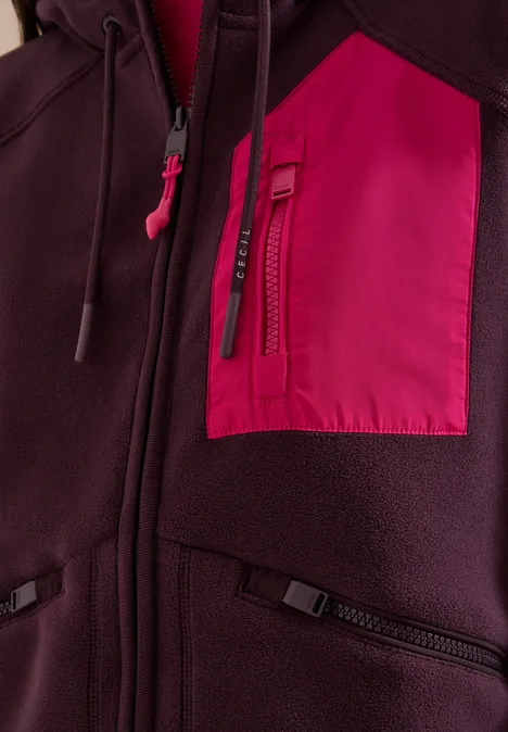 Nahaufnahme einer dunkelroten Fleecejacke mit pinker Brusttasche und Reißverschlüssen.