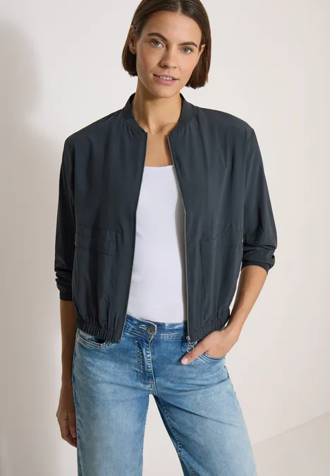 Femme porte une veste bomber bleu marine, un top blanc et un jean bleu.