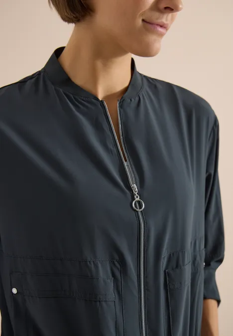 Gros plan d'une femme aux cheveux courts portant une blouse sombre zippée à col montant.