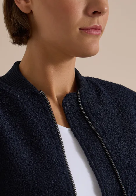 Close-up van persoon met wit T-shirt en donkerblauwe, gestructureerde jas met ritssluiting.