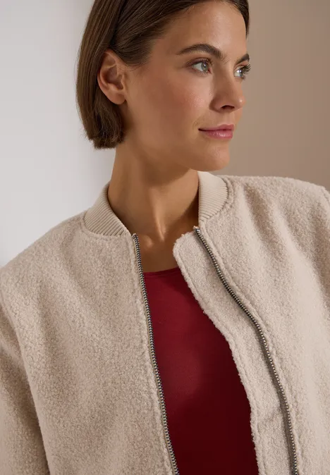 Eine Frau in beiger Teddy-Fleecejacke und rotem Top blickt seitlich.