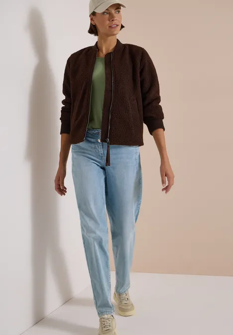 Blouson in Woll-Optik mit Zipper chocolate sauce brown Frau in dunkelbrauner Jacke, grünem Shirt, hellblauen Jeans, Sneakers und beigem Baseballcap vor schlichtem Hintergrund.
