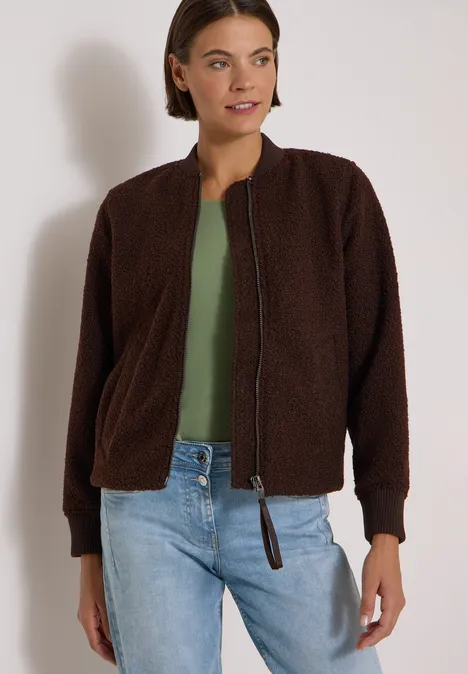 Blouson in Woll-Optik mit Zipper chocolate sauce brown Frau in brauner Teddy-Jacke, grünem Shirt und hellen Jeans vor neutralem Hintergrund.