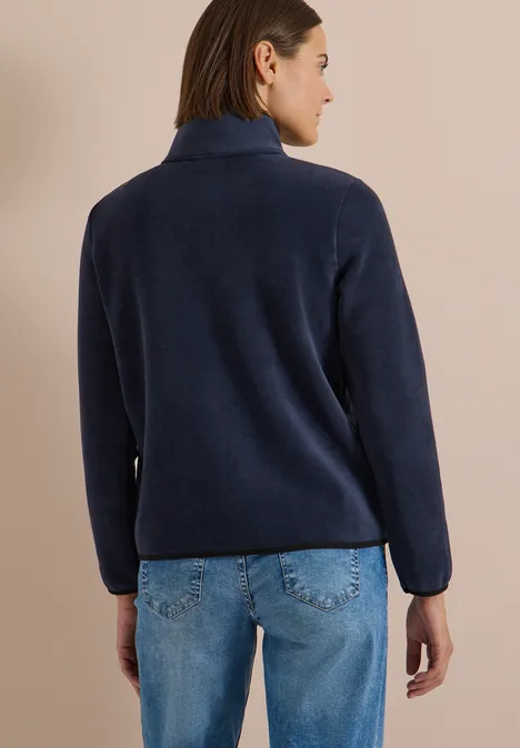 Frau steht mit dem Rücken zur Kamera und trägt einen dunkelblauen Fleece-Pullover und blaue Jeans.