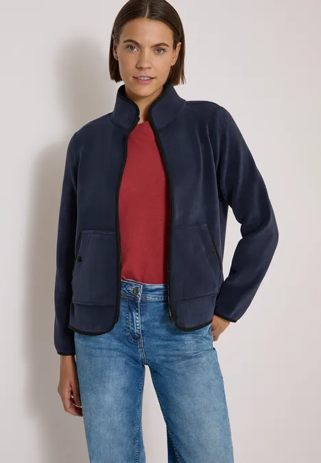 Junge Frau trägt dunkelblaue Fleecejacke, rotes Shirt und Jeans.