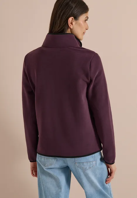 Vrouw van achteren met paarse fleecetrui en lichtblauwe spijkerbroek voor neutrale achtergrond.