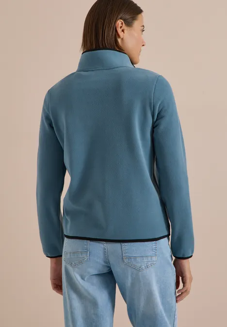 Rückansicht einer Frau in türkiser Jacke und Jeans.