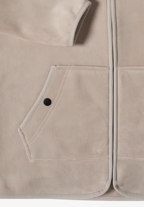 Nahaufnahme einer beigen Fleecejacke mit aufgesetzter Tasche und schwarzem Druckknopf.