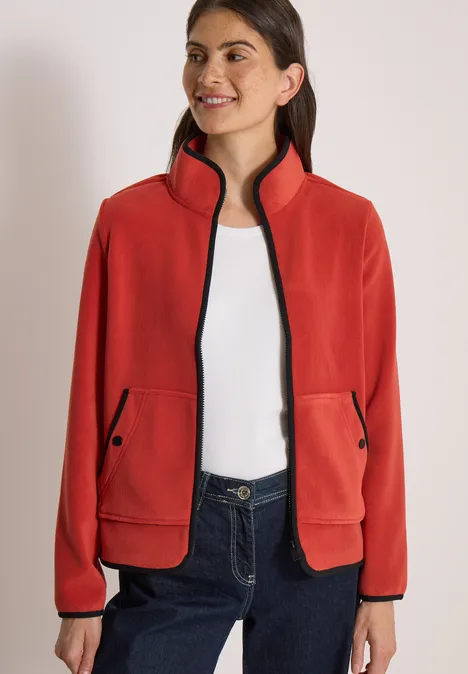 Model draagt rood fleecejack met opstaande kraag, zwarte accenten en steekzakken