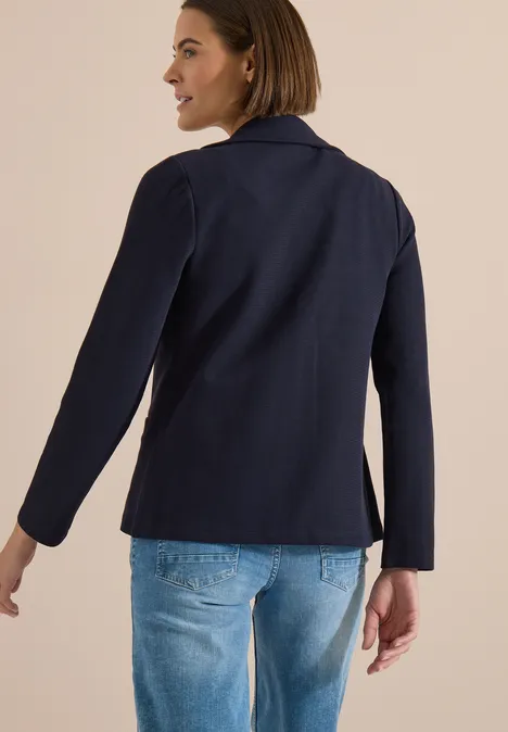Blazer mit Struktur in Unifarbe urban dark blue Rückansicht einer Person in dunkelblauer Jacke und hellblauen Jeans vor beigem Hintergrund.