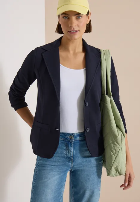 Blazer mit Struktur in Unifarbe urban dark blue Frau in dunkelblauer Jacke, weißem Top, Jeans und grünem Stoffbeutel.
