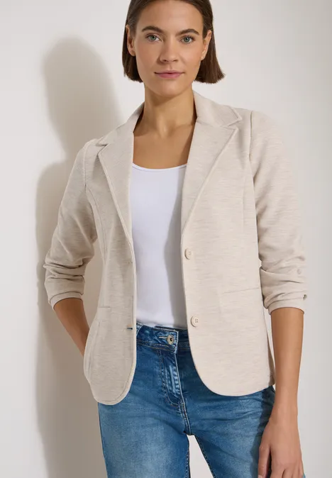 Blazer texturé, couleur unie cashmere beige melange Frau in hellbeigem Blazer, weißem Top und blauen Jeans, lässige Pose mit Händen in den Taschen.