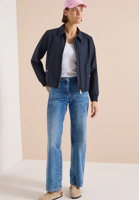 Kurtka Blouson z kołnierzem koszulowym urban dark blue Kobieta w granatowej kurtce, białym T-shircie i niebieskich dżinsach na jasnym tle.