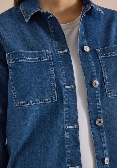 Blaue Jeansjacke mit zwei Brusttaschen über weißem T-Shirt.