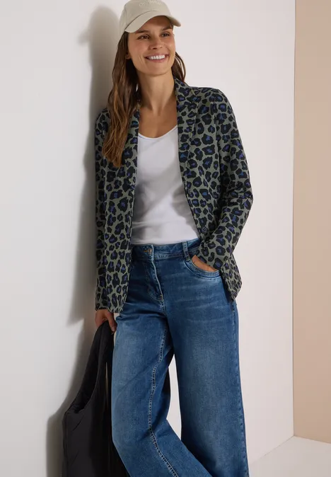 Blazer ample à boutons et imprimé dried olive green Femme décontractée appuyée contre un mur en blazer léopard, t-shirt blanc, jean large et casquette.