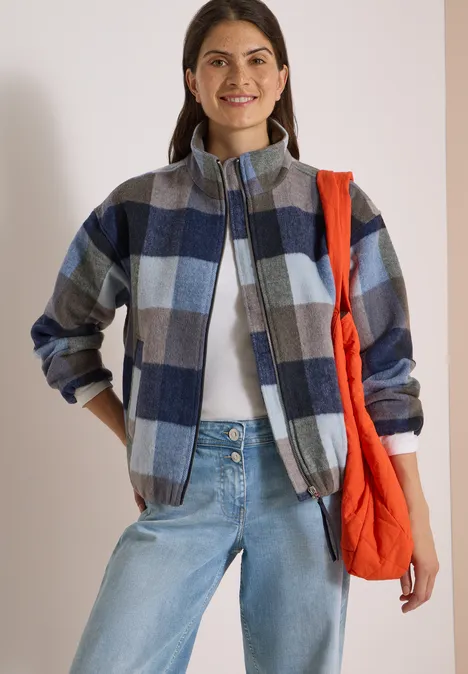 Blouson à col montant et motif à carreaux urban dark blue Femme en veste à carreaux bleu-gris, t-shirt blanc, jean clair et sac rouge porté sur l'épaule