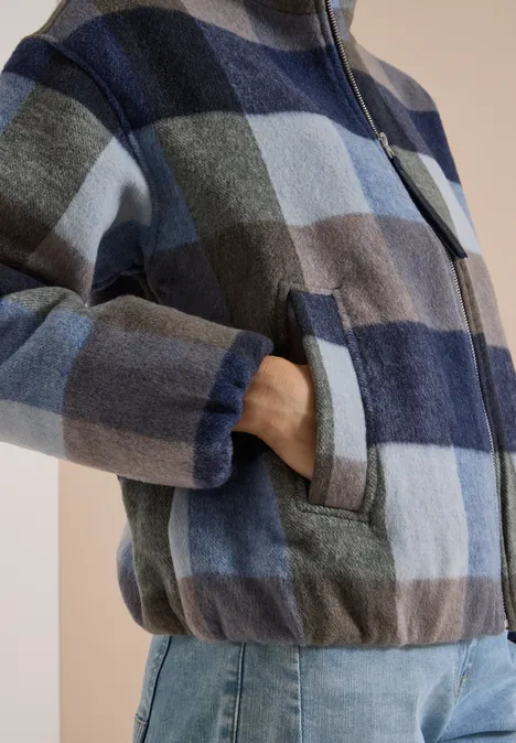 Blouson à col montant et motif à carreaux urban dark blue Personne porte une veste à carreaux bleus avec fermeture éclair et poches, et un jean.